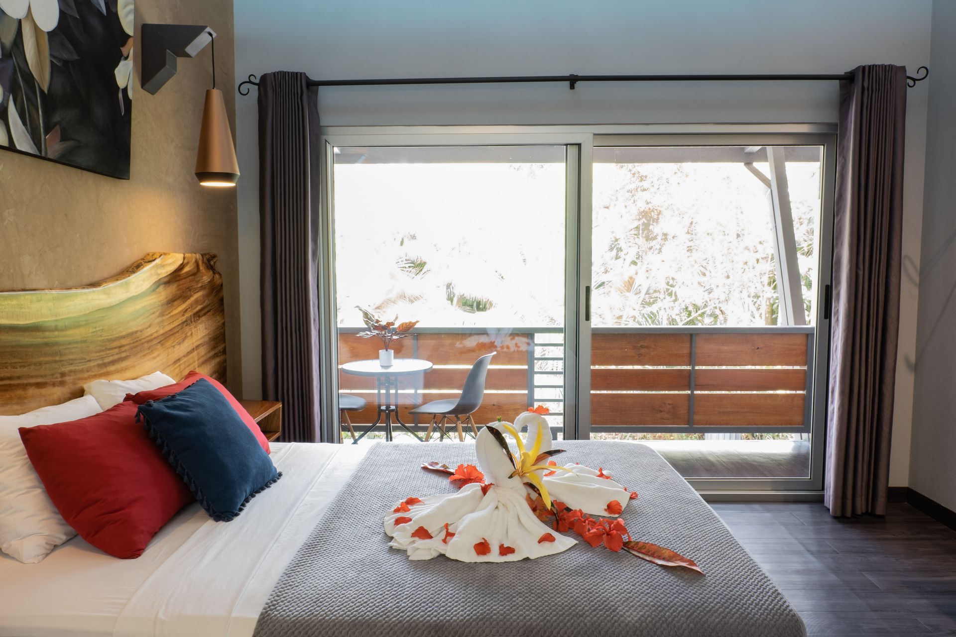 A hotel room featuring a bed with towel swans, a natural wood headboard, and sliding glass doors opening to a balcony.