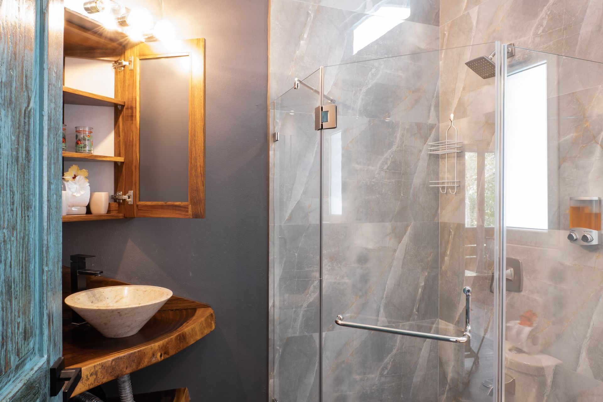 A rustic bathroom with a live-edge wood vanity, vessel sink, and a modern glass-enclosed shower with gray stone tiles.