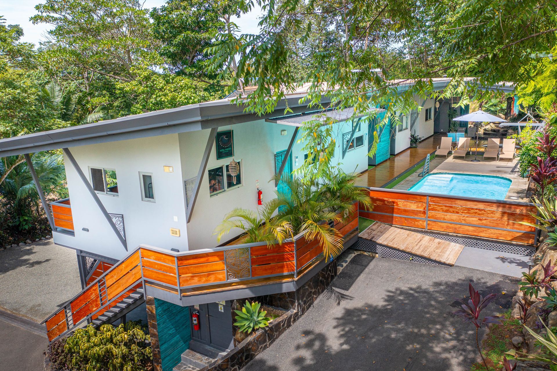 A modern, white multi-level building with wood accents and stairs, nestled in lush greenery next to a small swimming pool.