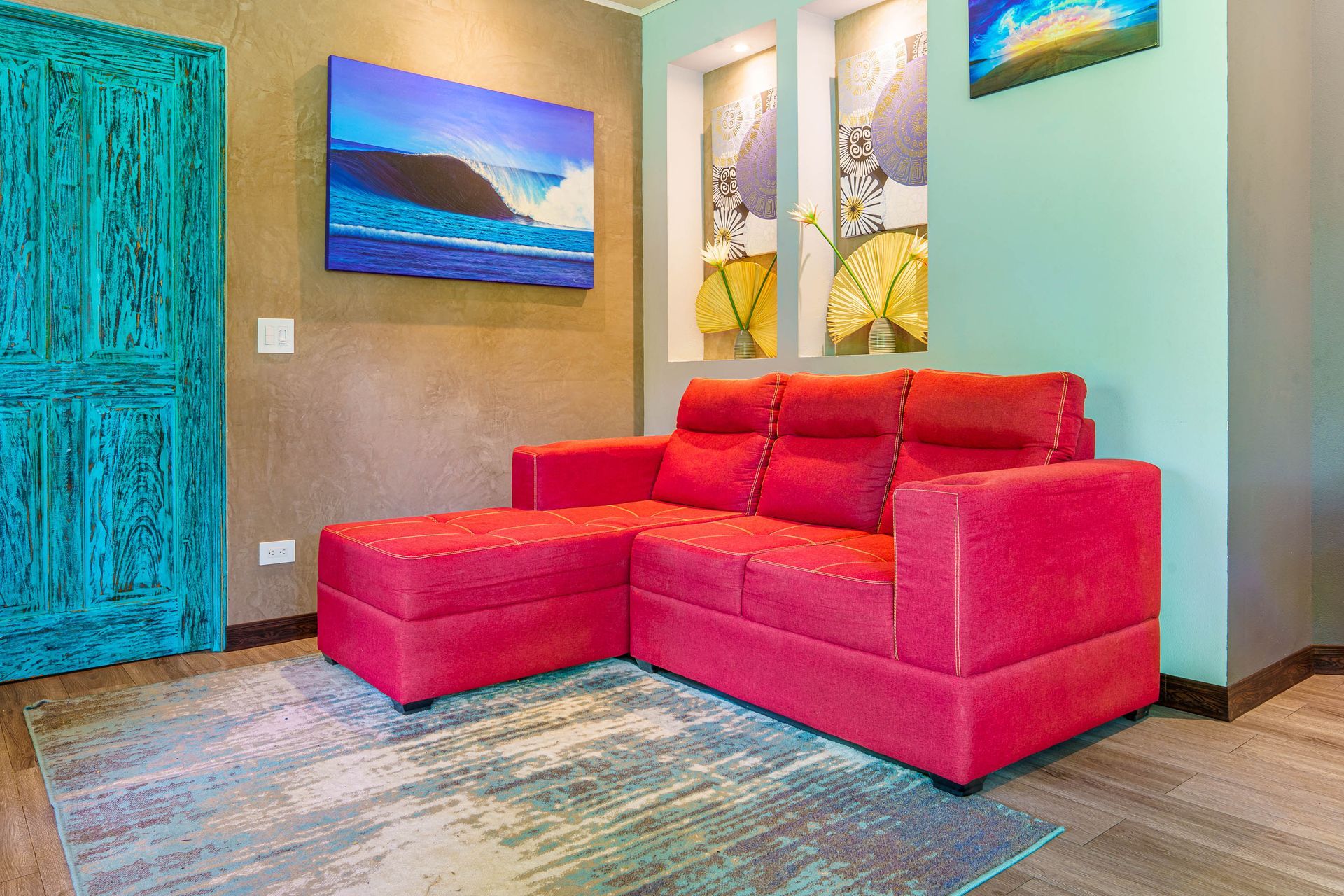 Bright red sectional sofa in a colorful living room with teal walls and abstract wall art