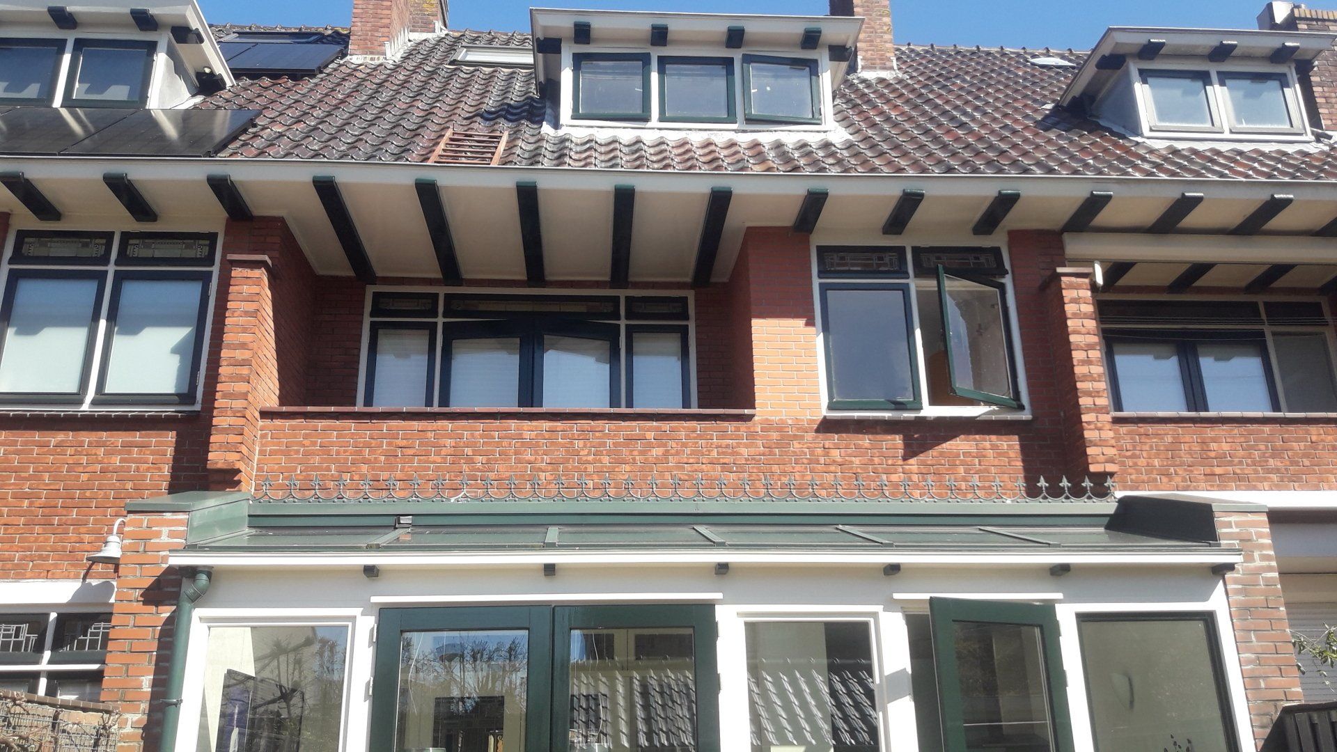 Gevel van een rijtjeshuis van baksteen met donker omlijste ramen en een groene luifel boven de ingang.