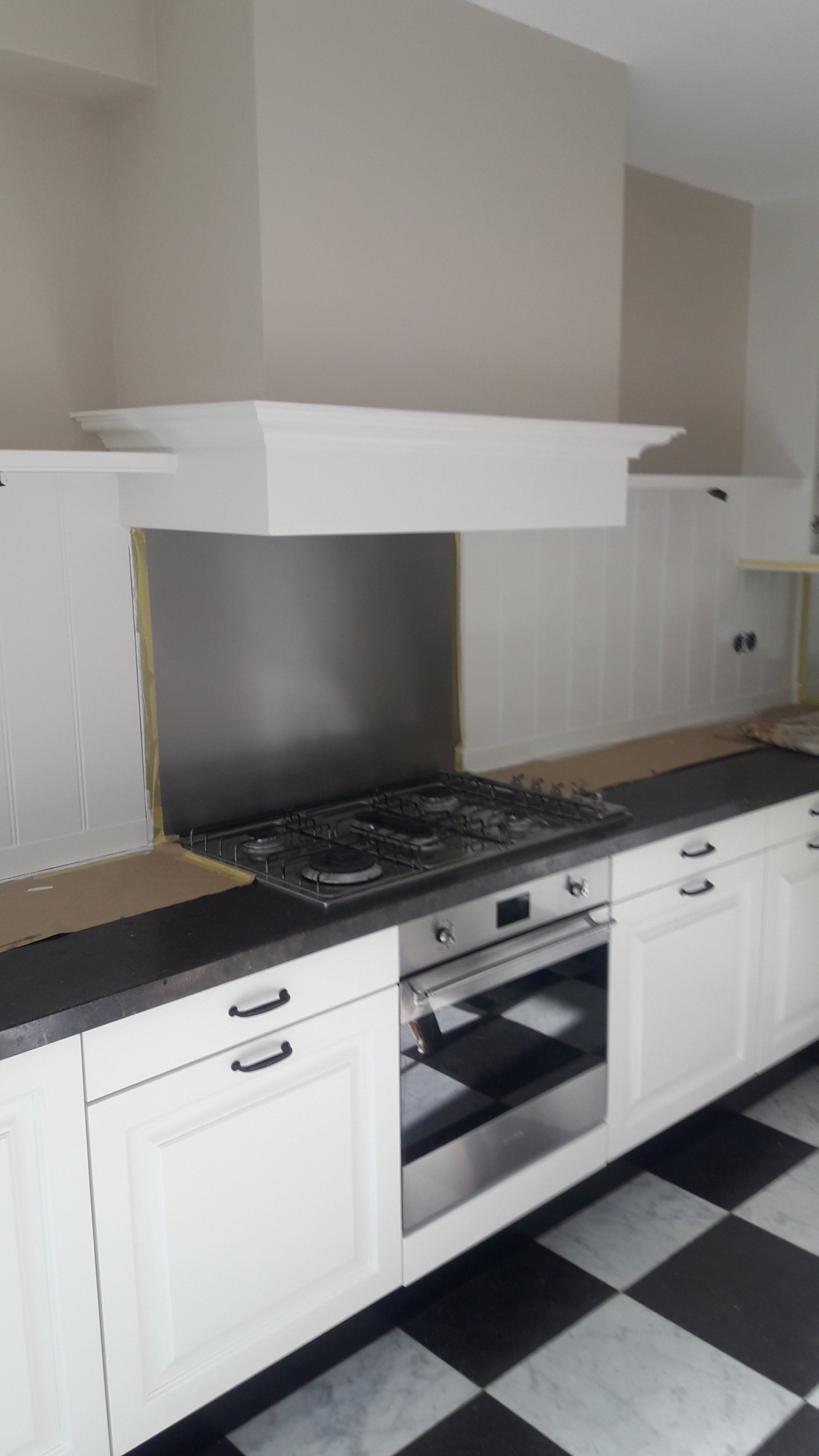 Witte keuken met geblokte vloer, roestvrijstalen fornuis en afzuigkap, en witte keukenkastjes.