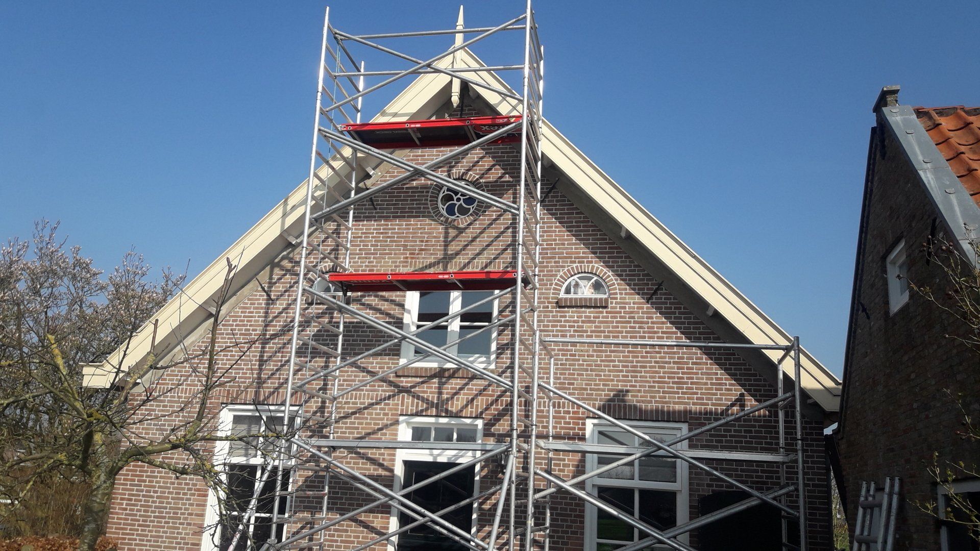 Huis in renovatie met steigers, voorgevel zichtbaar.