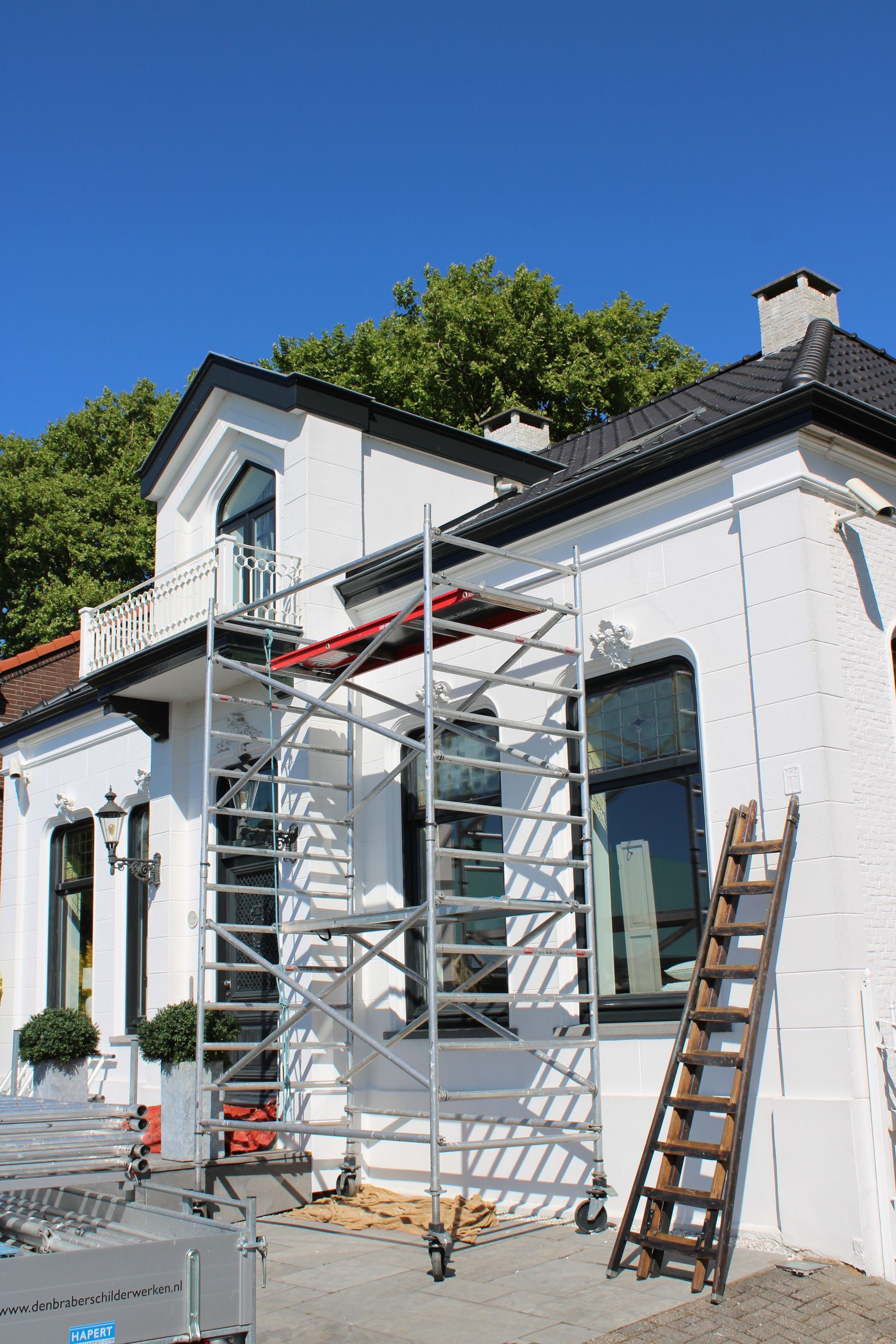 Het witte huis wordt geschilderd, met steigers en een ladder tegen de voorgevel.
