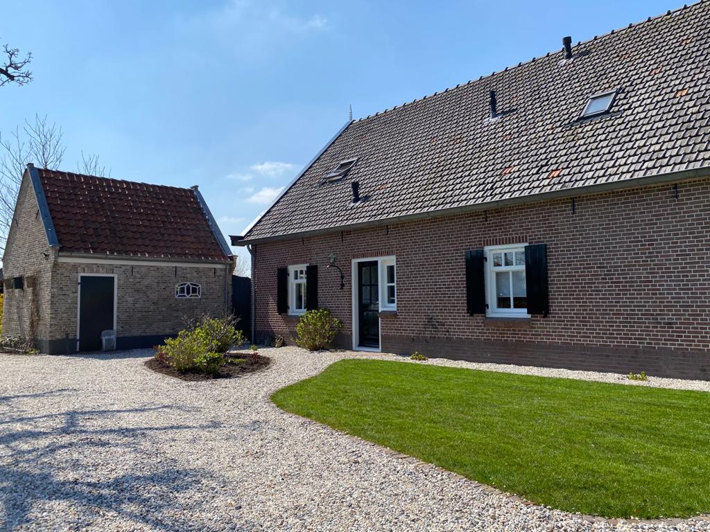 Een bakstenen huis met een vrijstaande garage, een grindoprit en een klein groen gazon onder een blauwe hemel.