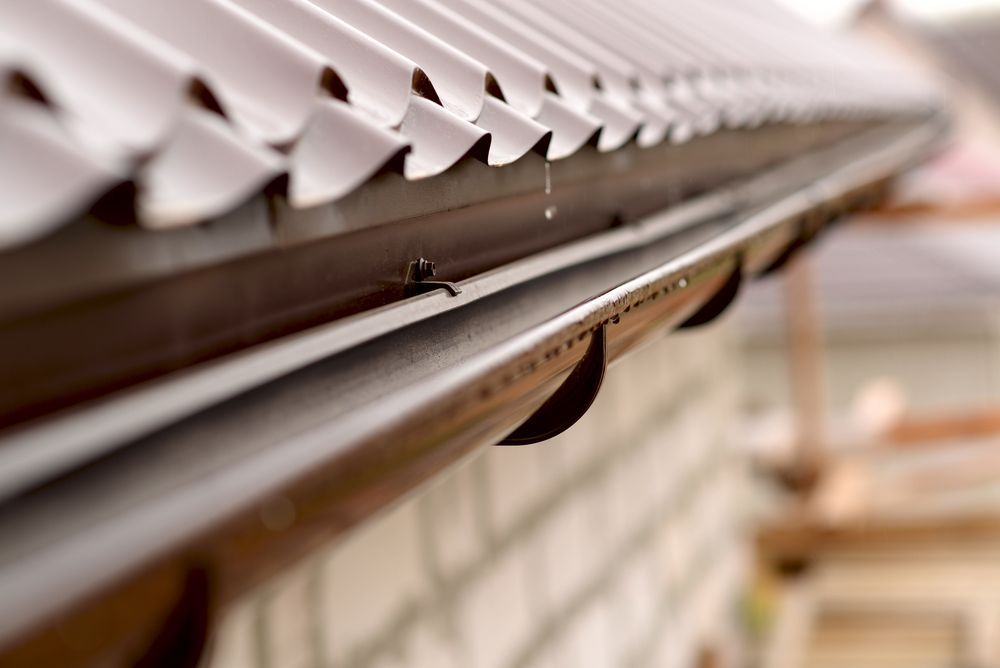Brown Gutters Attached to a Corrugated Metal Roof. a Few Water Droplets Hang — Coffs Coast Roofing In Mullaway, NSW