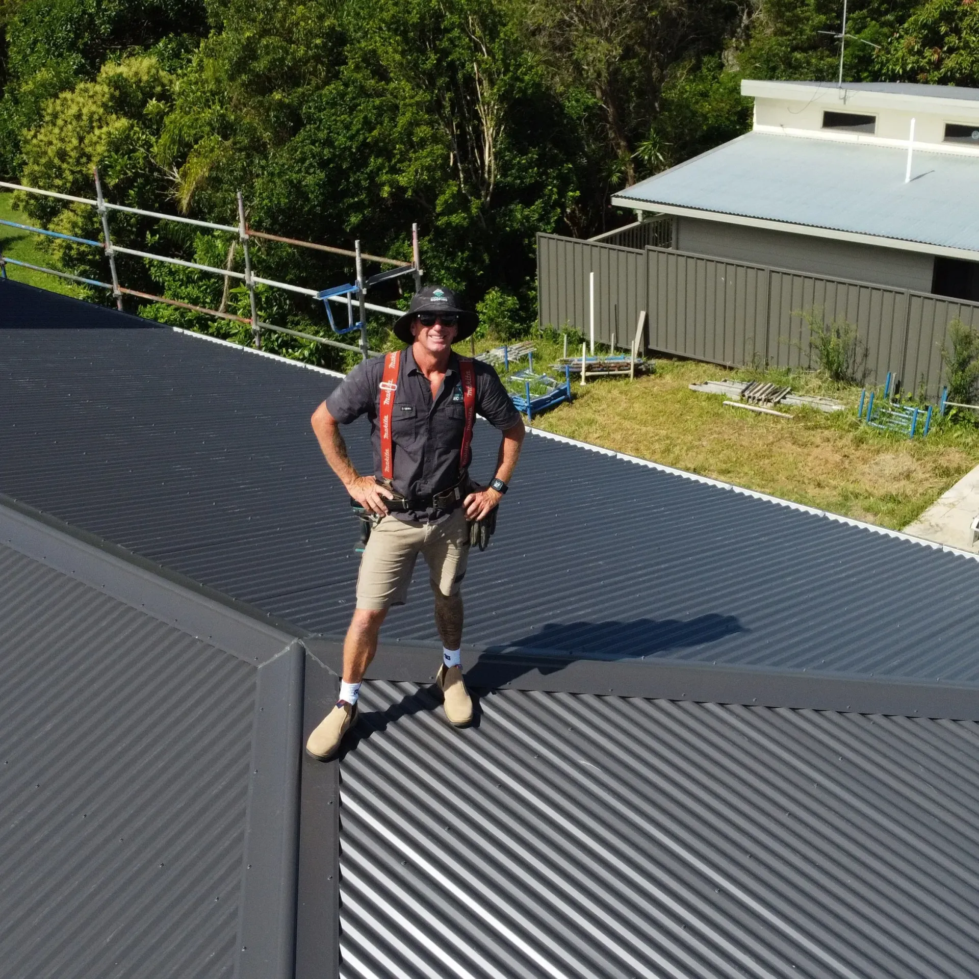Person standing on corrugated metal roof, wearing safety gear; sunny day.