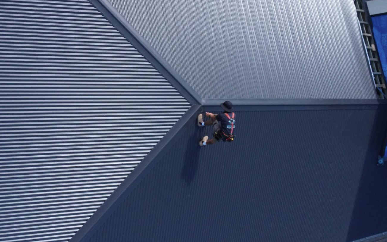 Person in red and blue athletic gear walking on a dark blue surface. Metallic roof overhead.
