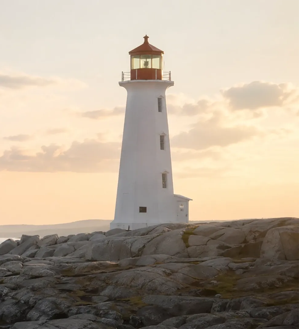 Weißer Leuchtturm an felsiger Küste im Sonnenuntergang, dahinter ein warmer, goldener Himmel