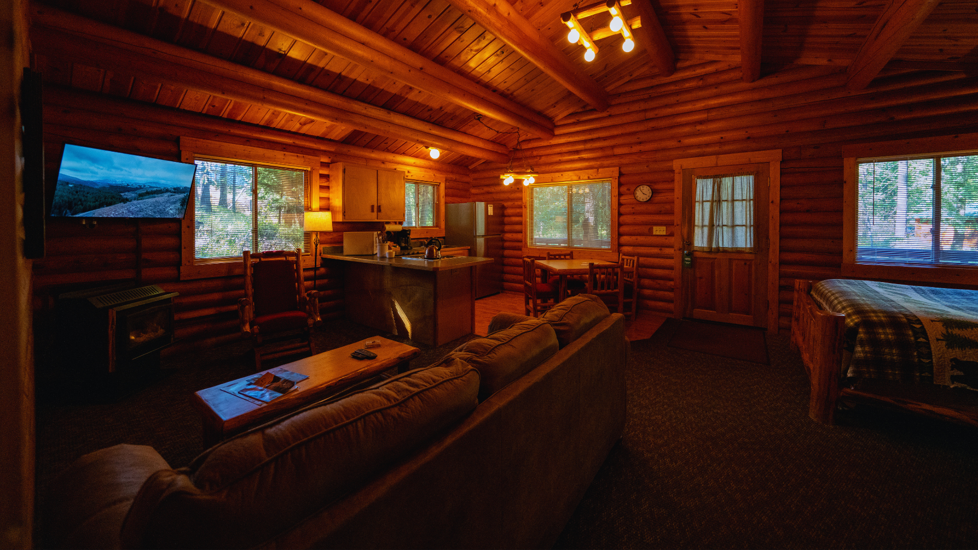 Warm log cabin living room with wood walls, couches, fireplace, and large windows showing snowy outdoors
