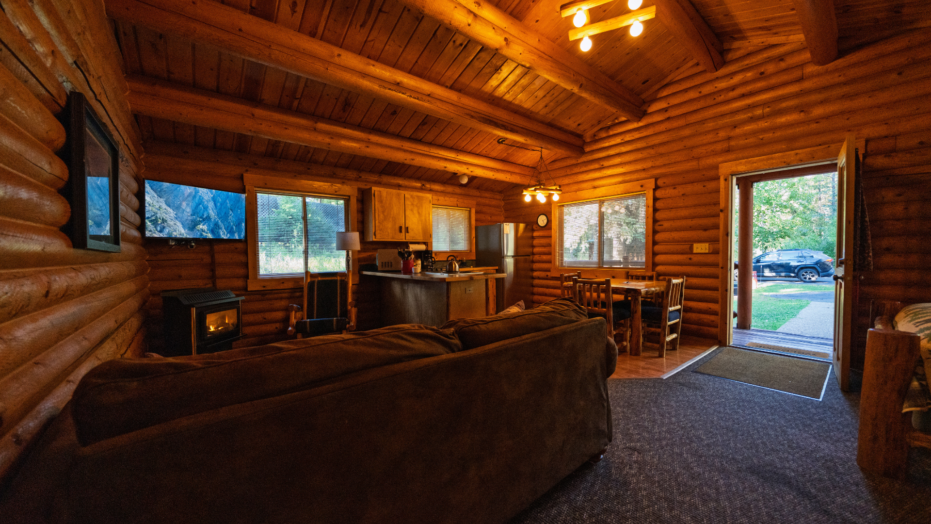 Rustic log cabin living room with wood-paneled walls, sofa, fireplace, and view through open doorway