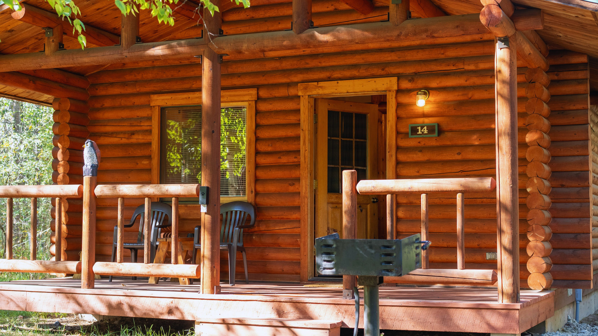 Wooden cabin porch with log railings, chairs, and a small table in a forest setting