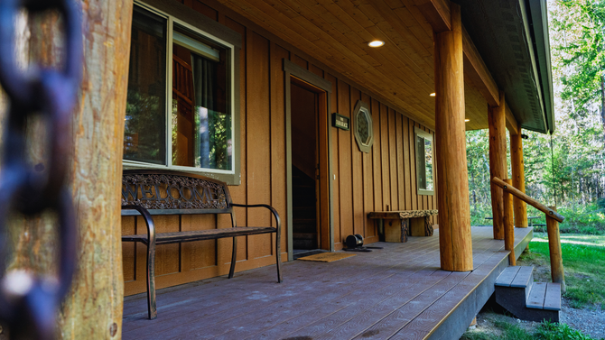 Wooden cabin porch with benches, columns, and a railing overlooking greenery