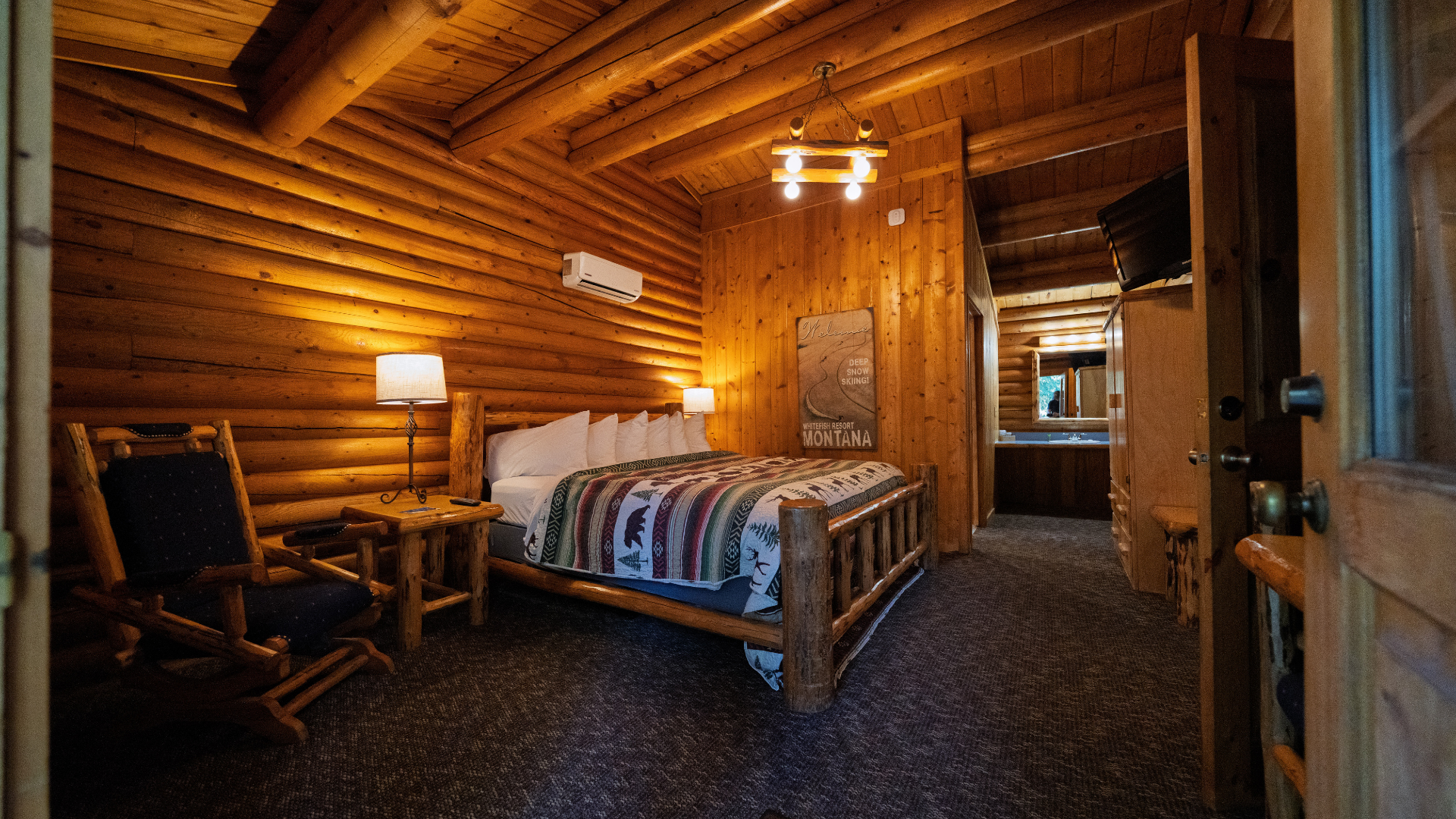 Rustic log cabin bedroom with a bed, nightstand, warm lighting, and wooden walls