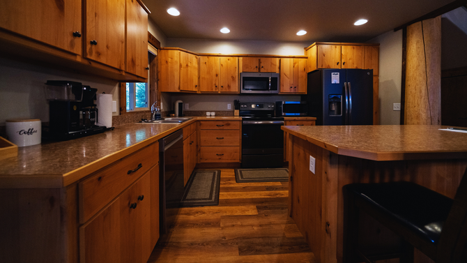 Warm wooden kitchen with cabinets, island, black appliances, and recessed ceiling lights.