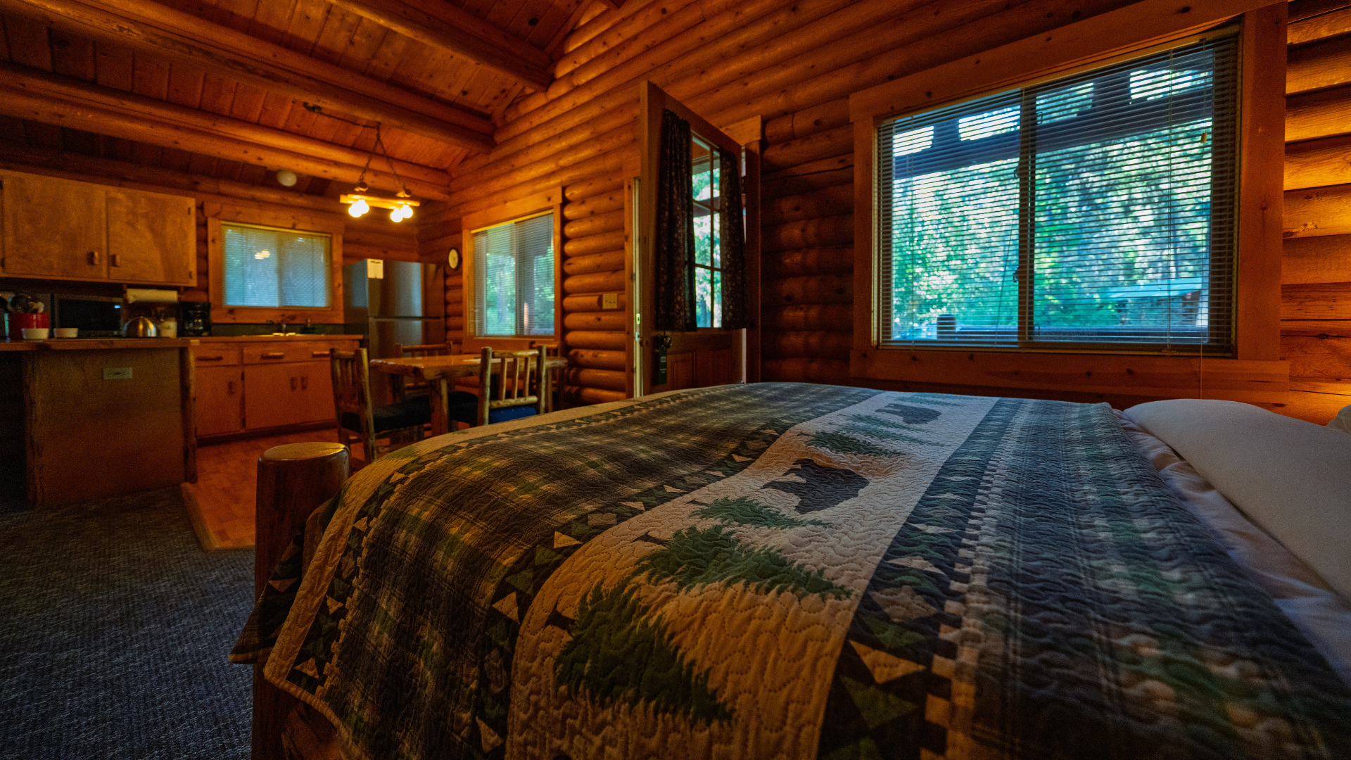 Cozy log cabin bedroom with quilted bed, wood-paneled walls, and large windows overlooking trees