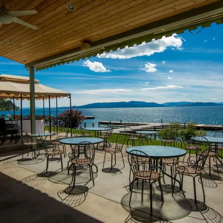 A patio with tables and chairs overlooking a lake