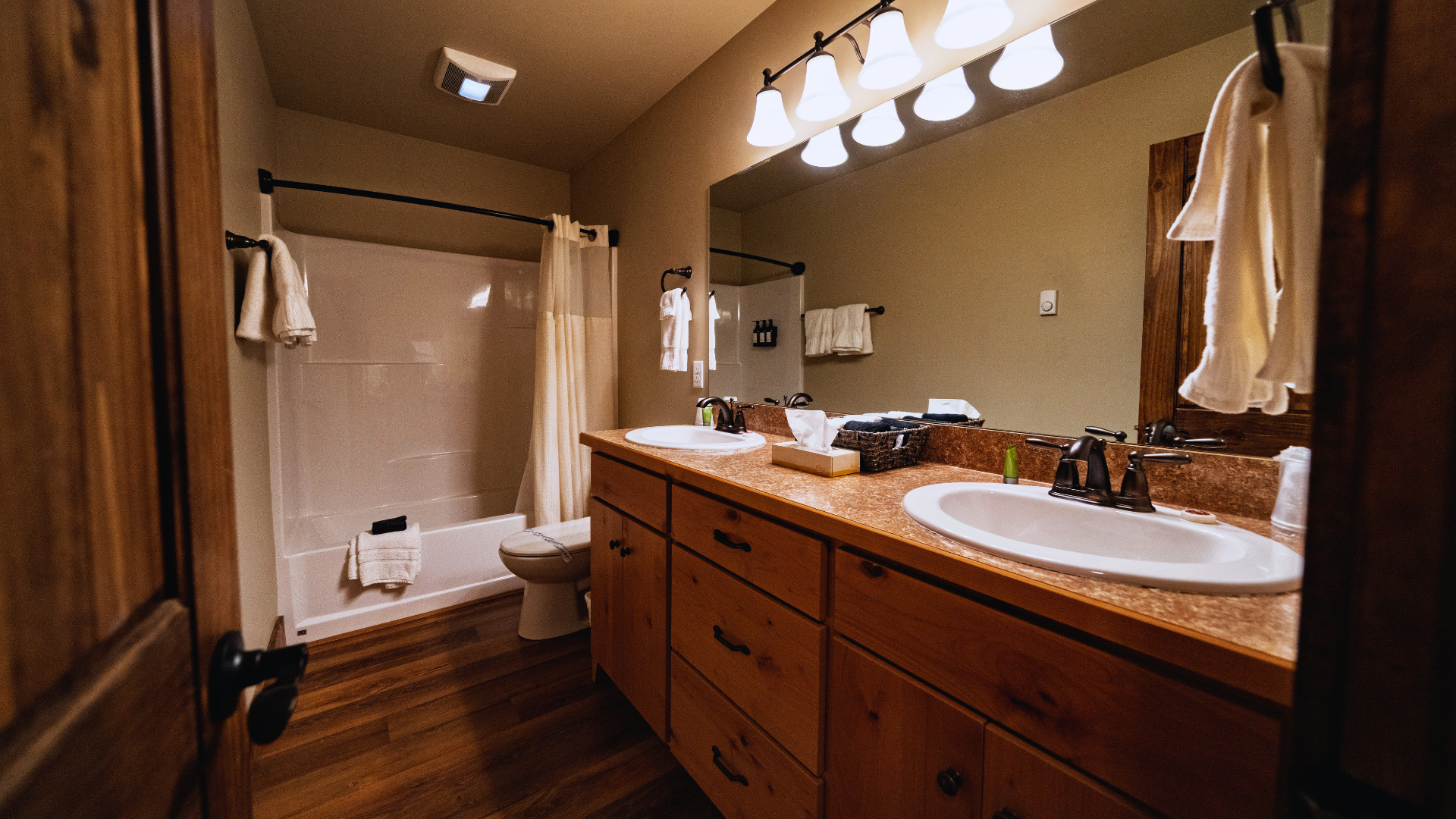 Warm bathroom with double vanity, large mirror, and a tub-shower area behind a curtain.