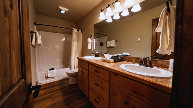 Warm bathroom with double sink vanity, mirror lights, toilet, and shower curtain.