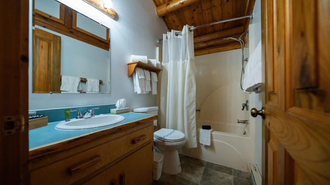 Small rustic bathroom with wood cabinets, blue sink counter, toilet, shower curtain, and bathtub.
