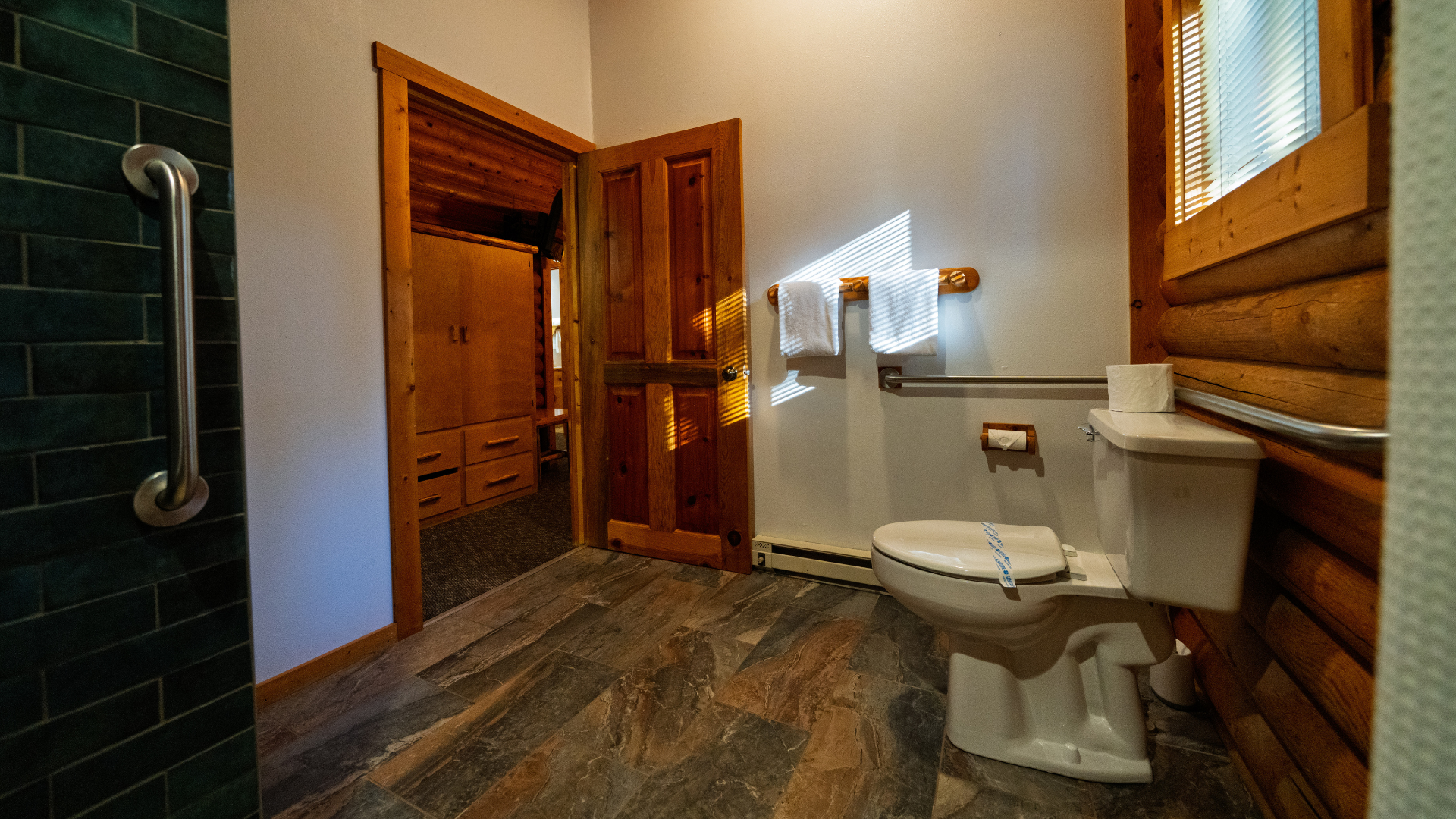 Rustic bathroom with wood walls, white toilet, dark tile floor, and a walk-in shower visible through open door