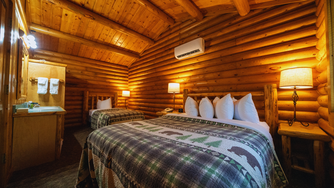 Cozy log cabin bedroom with a large bed, warm lamp light, and wooden walls and ceiling