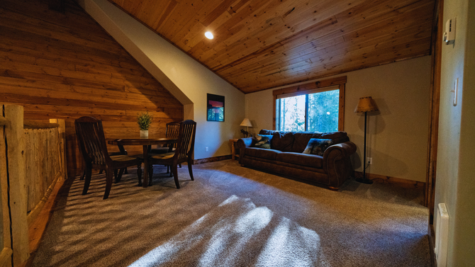 Cozy attic living room with wood ceiling, carpet, sofa, dining table, and large window light