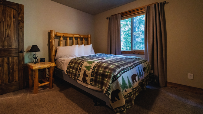 Cozy bedroom with log bed, patterned quilt, bedside lamp, and window with curtains