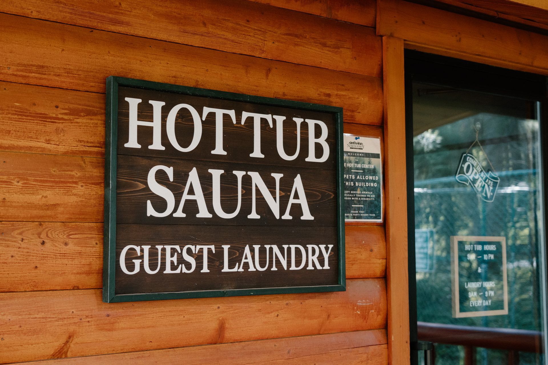 A wooden sign on the side of a log cabin says hot tub sauna guest laundry.
