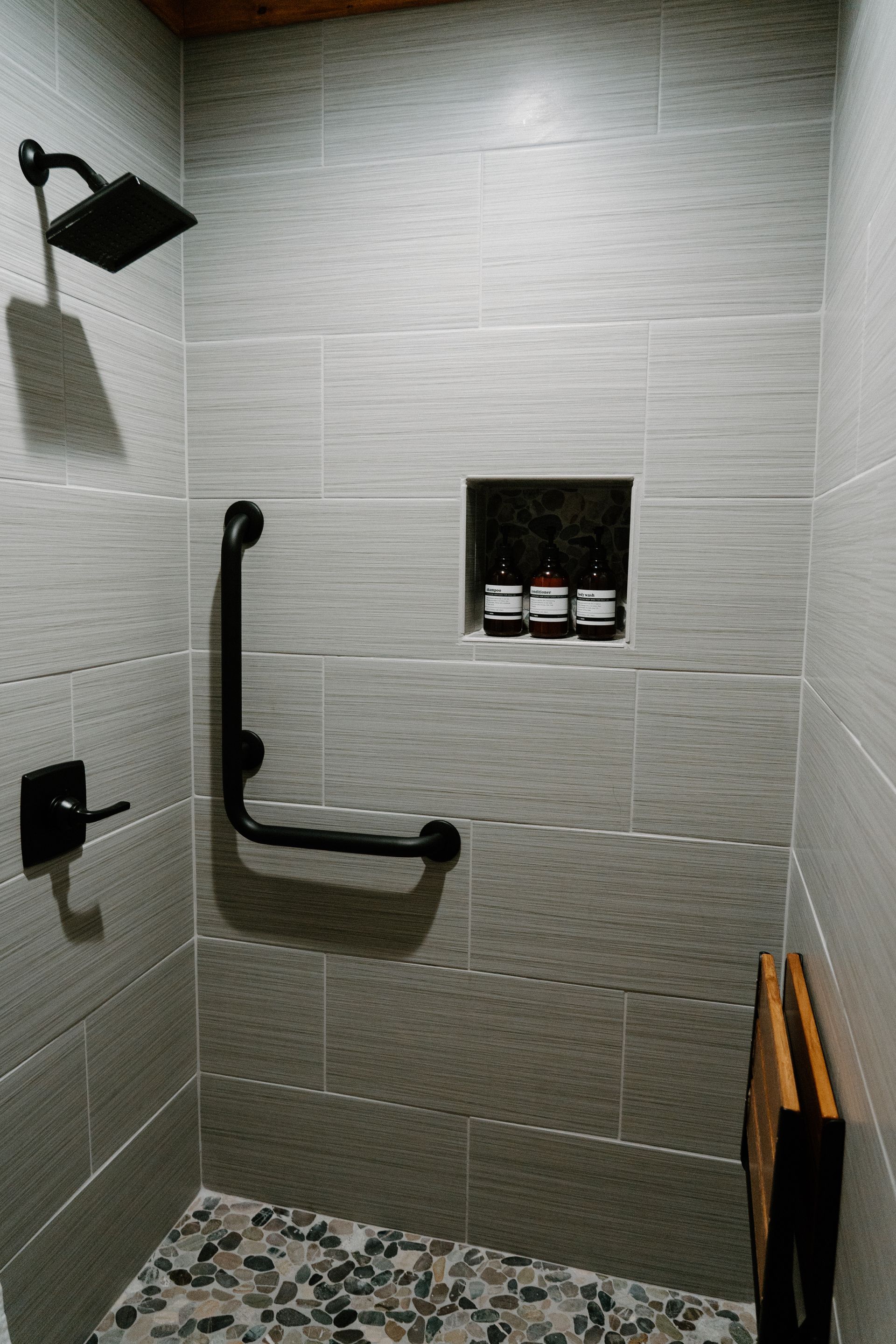 A walk in shower with a hand rail and a shower head.