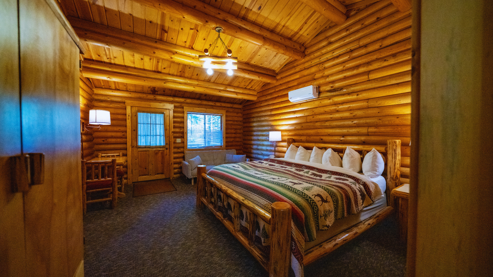 Cozy log cabin bedroom with wooden walls, a double bed, windows, and warm overhead lighting