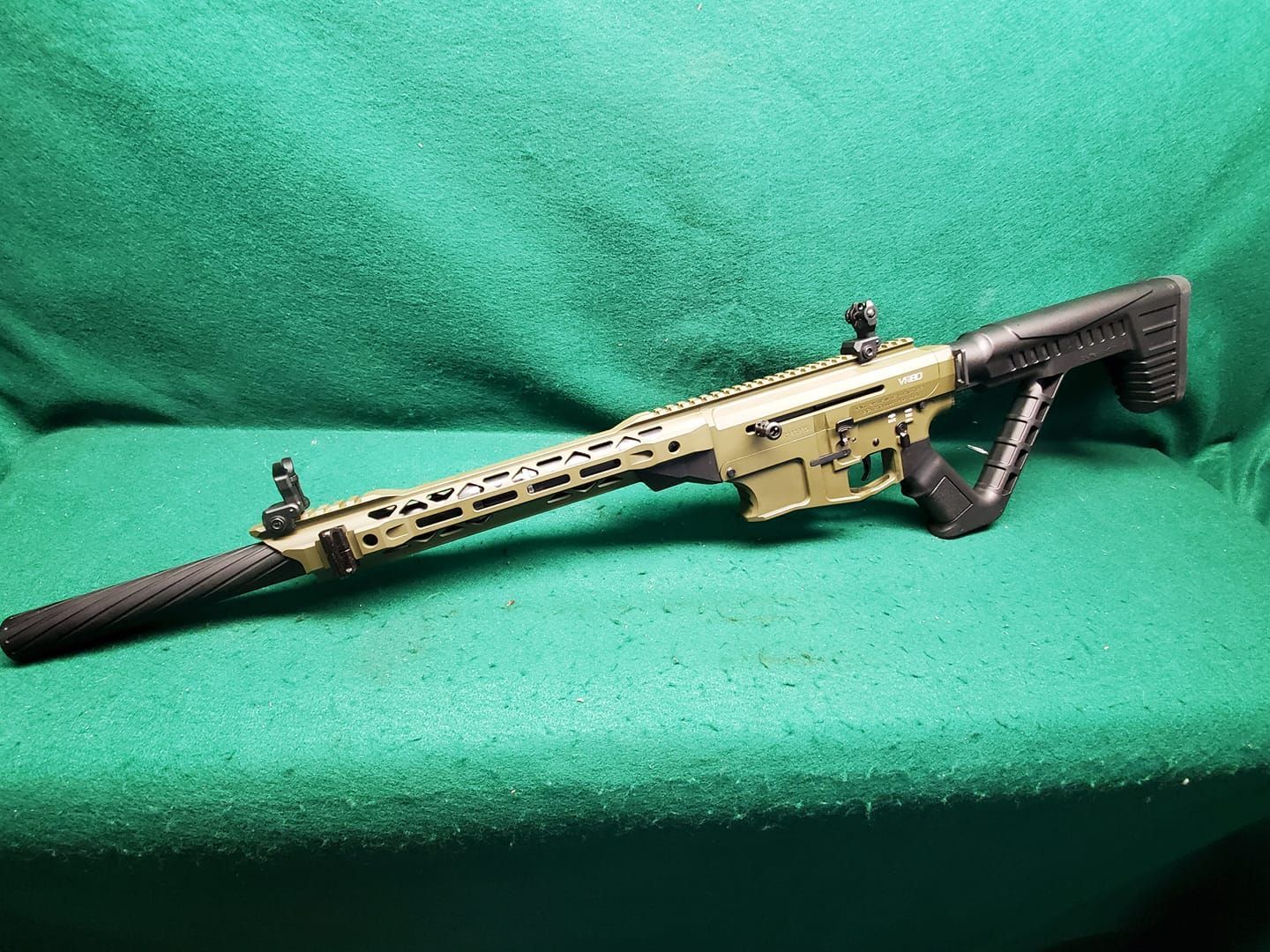 Olive-green rifle on a green surface. Features a long barrel, stock, and sights.