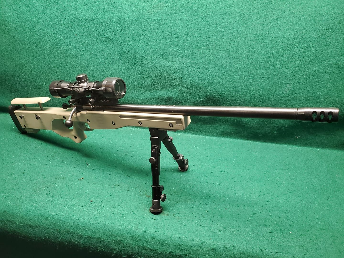 Tan and black sniper rifle with a scope, mounted on a bipod, against a green background.