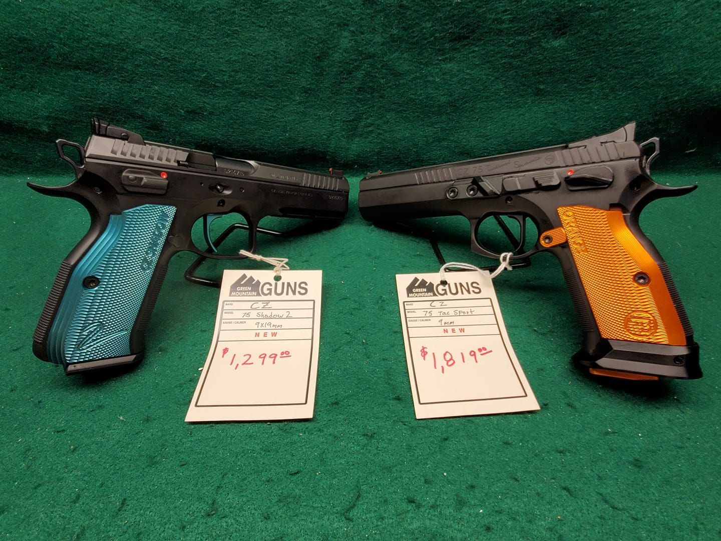 Two black handguns with colored grips, labeled with price tags, on green surface.