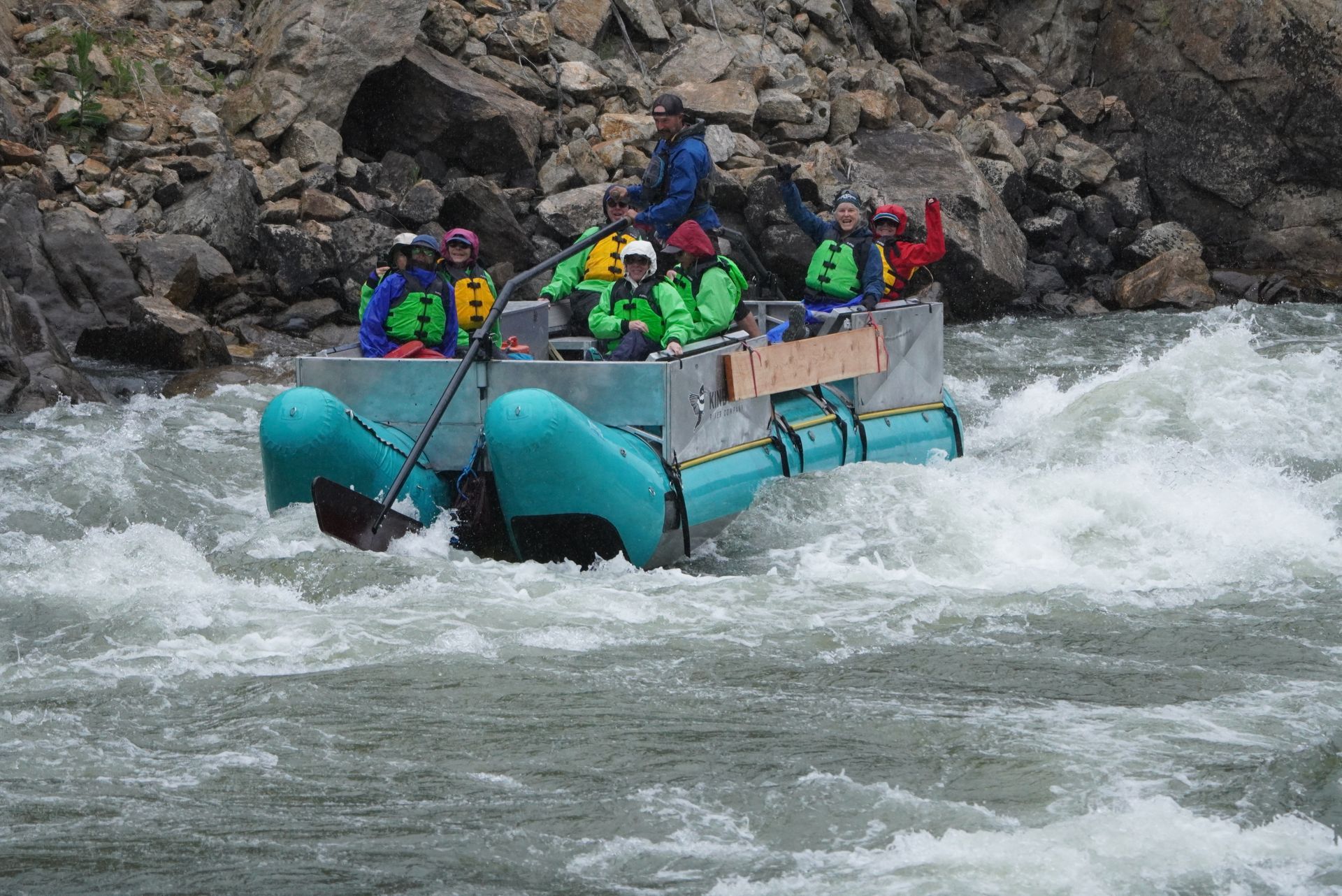 Rafting group in colorful helmets and life jackets navigating rough whitewater near rocky riverbank