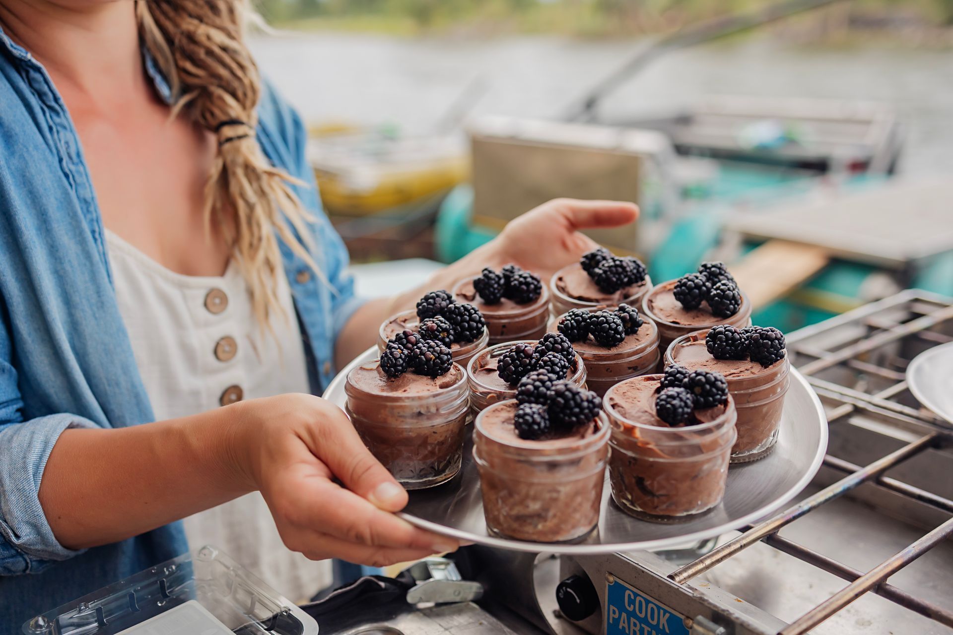 Person presenting chocolate dessert cups topped with berries on a tray outdoors