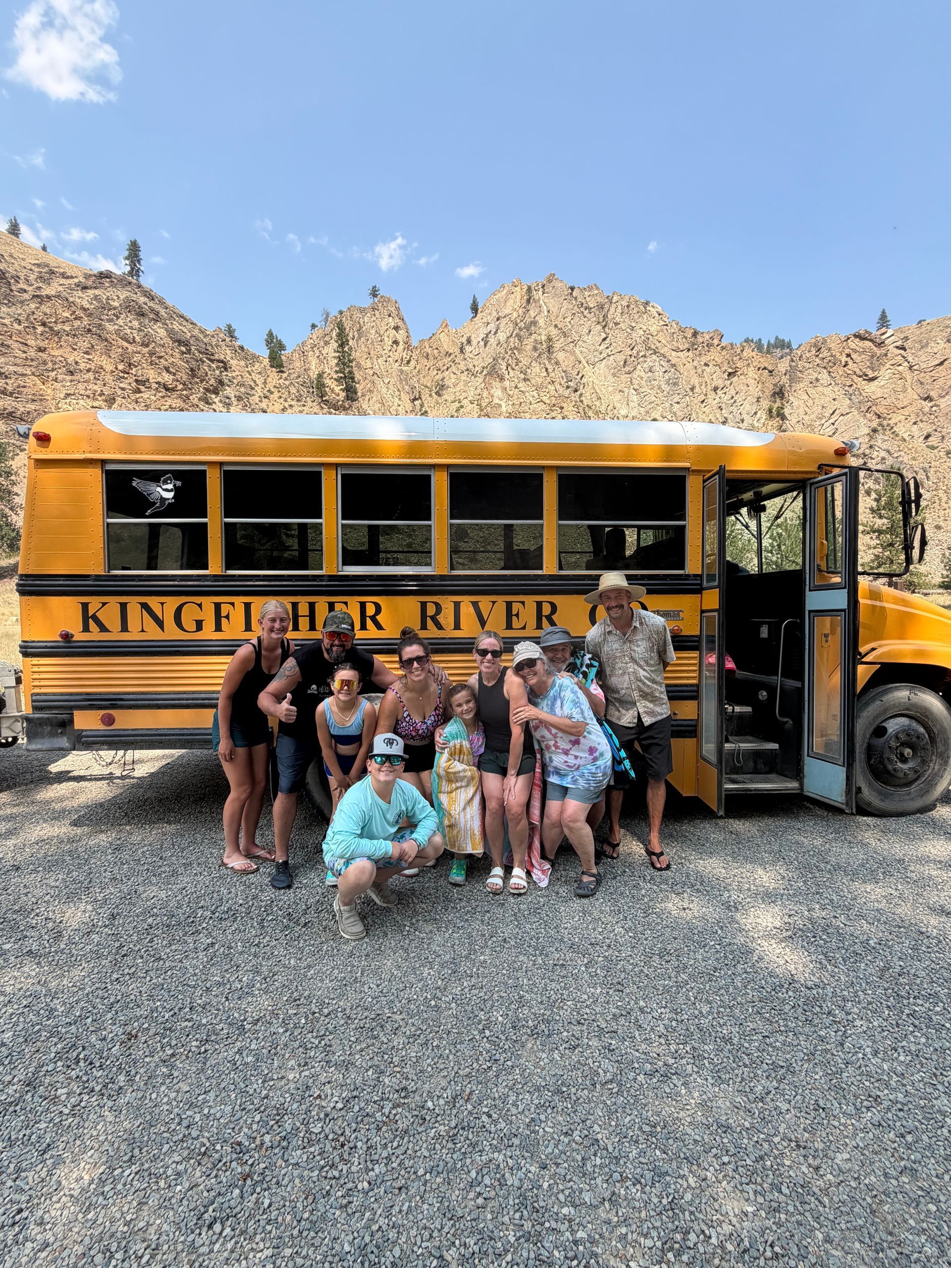 Group posing by a yellow school bus in a rocky desert setting under a clear blue sky