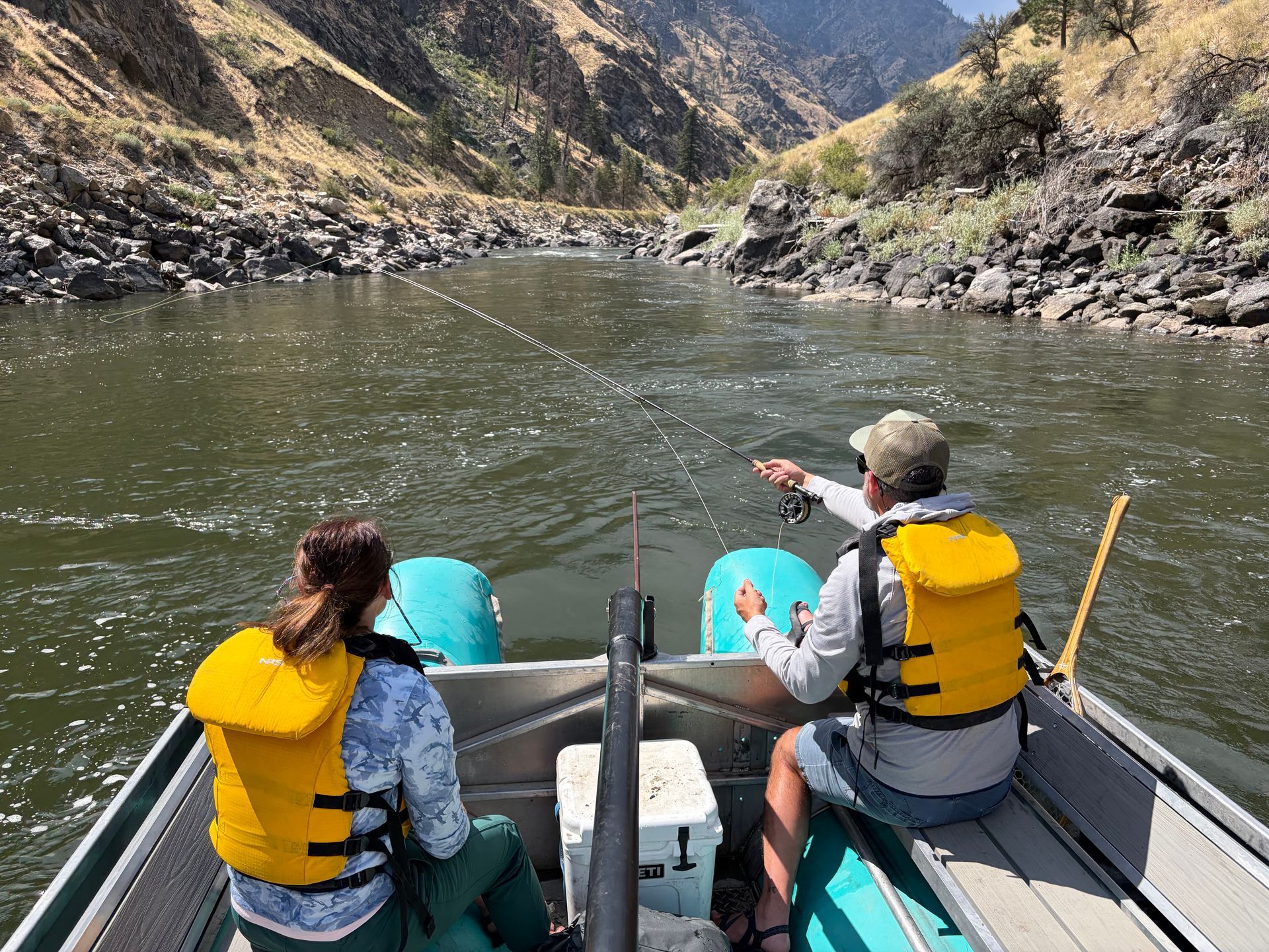 Two people in yellow life jackets rafting on a river through a rocky canyon