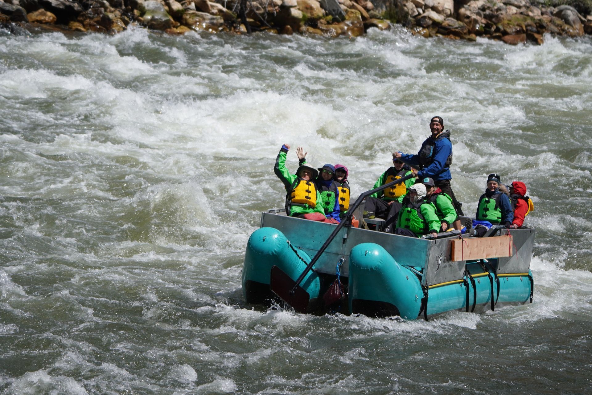 People rafting on rough river rapids in a teal inflatable raft