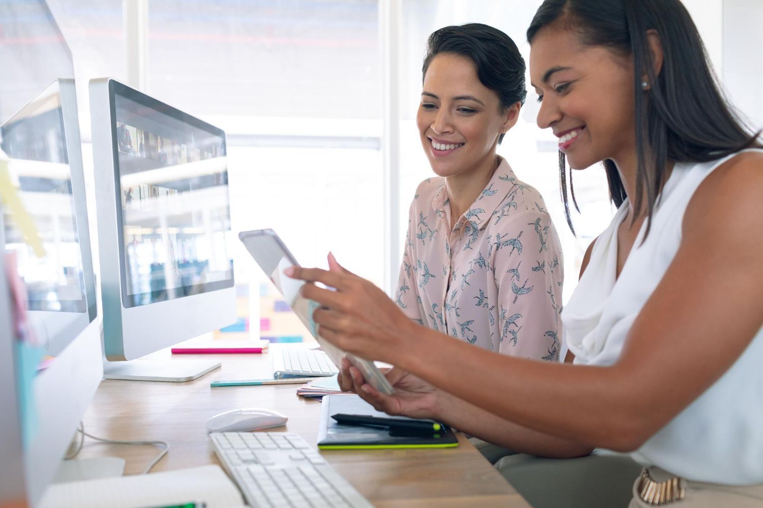 Dos mujeres están sentadas en un escritorio mirando una tableta.