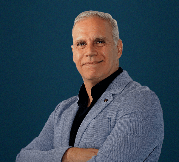 Un hombre con una chaqueta azul y una camisa negra está de pie con los brazos cruzados.