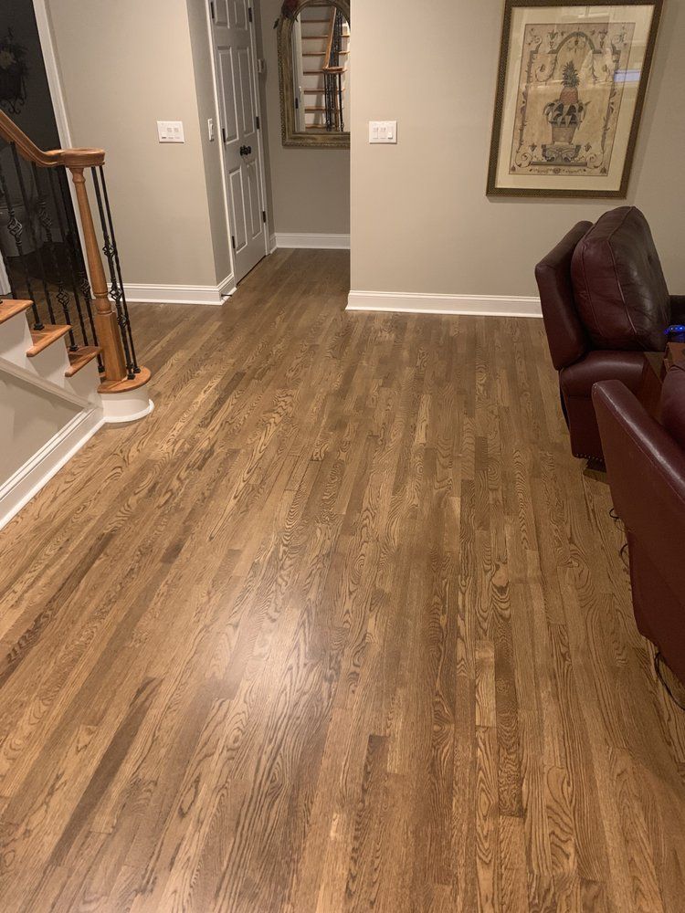 A living room with hardwood floors , stairs , chairs and a picture on the wall.