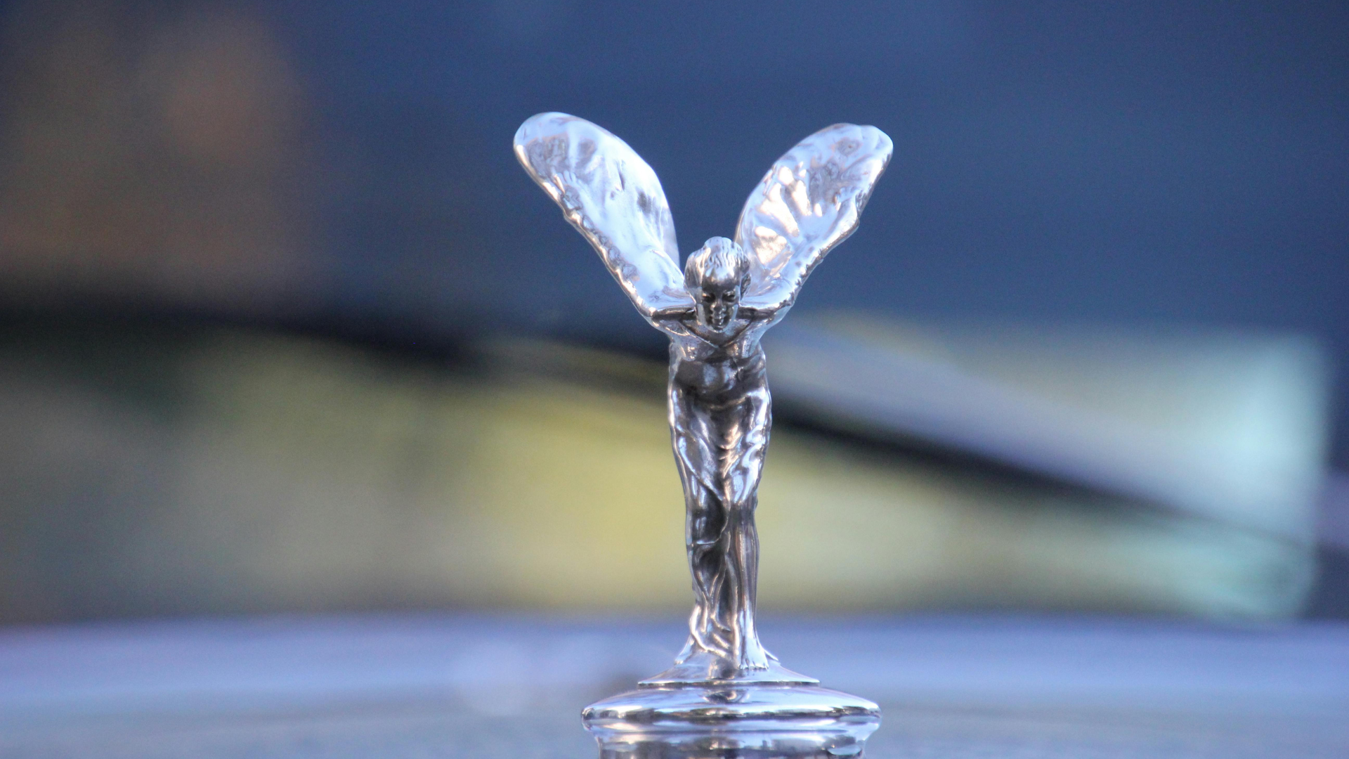 Small silver fairy figurine with clear wings standing on a reflective surface against a blurred background