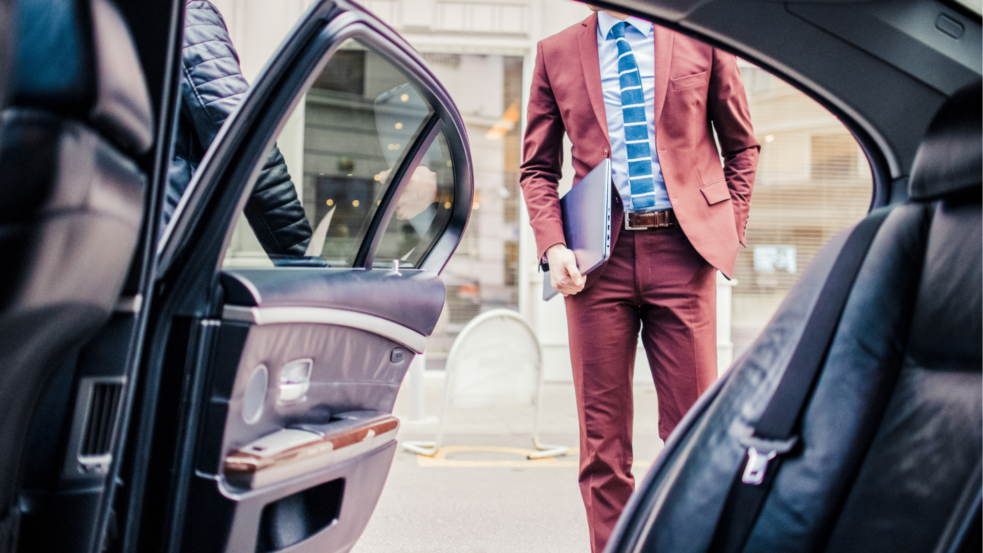 Man in a maroon suit standing beside an open car door, viewed from inside the vehicle.