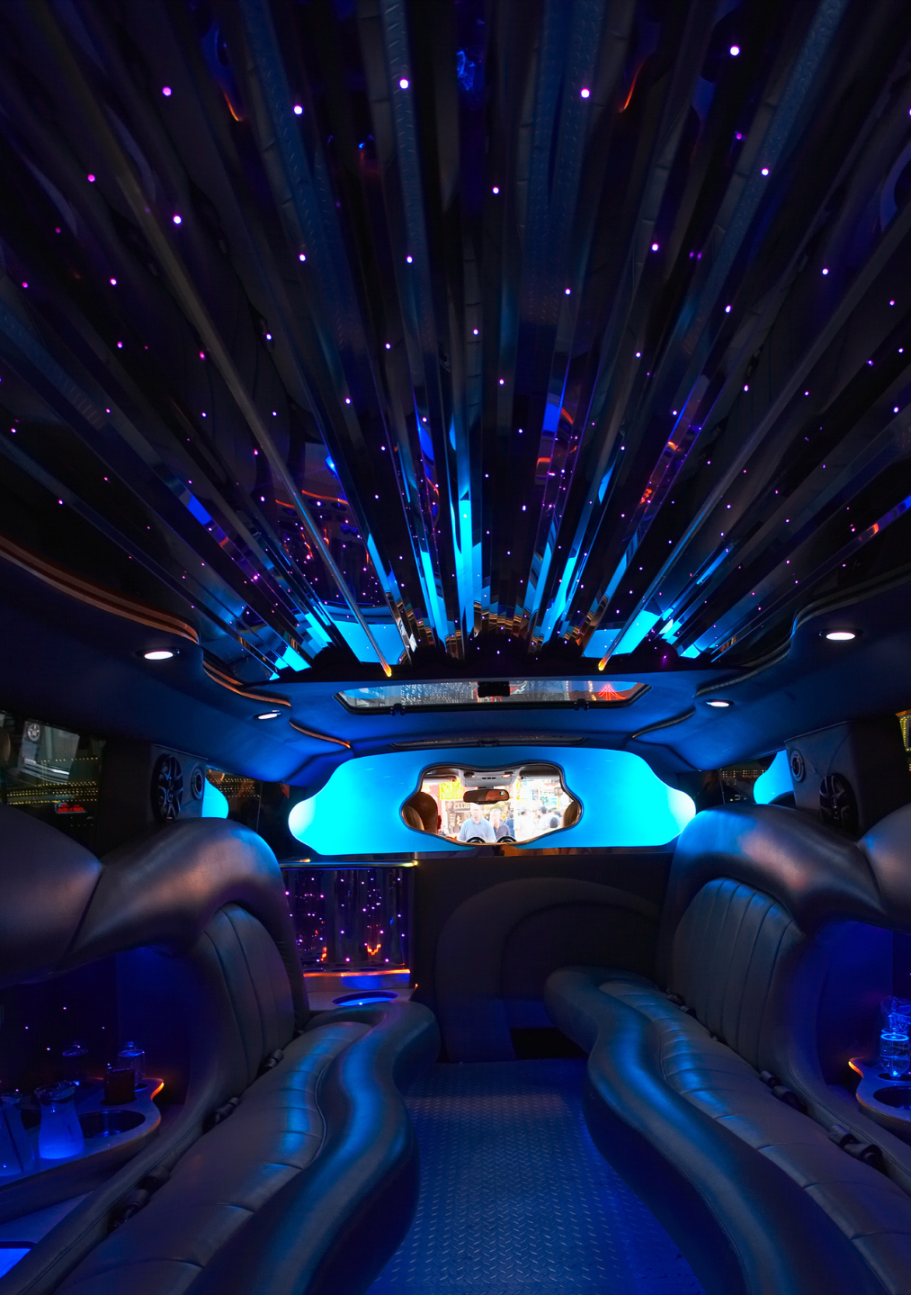 Interior of a luxury limousine with blue LED lights and starry ceiling, viewed from the back seat