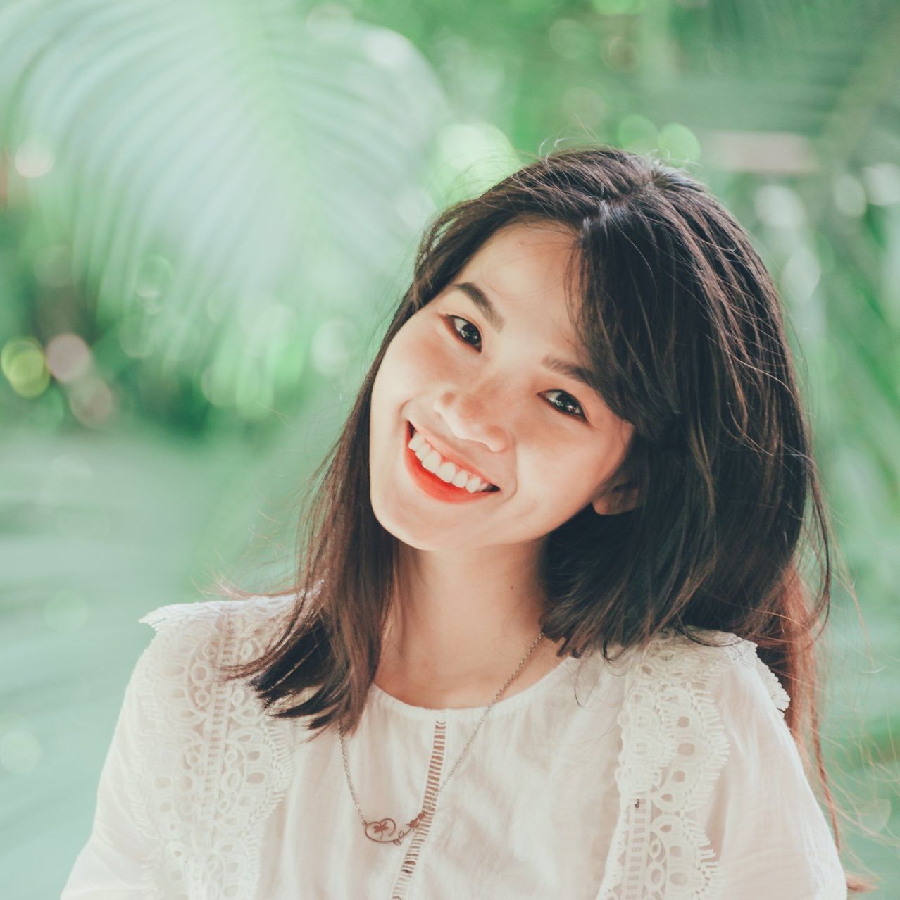 一位身穿白襯衫、戴著項鍊的女子正對著鏡頭微笑。