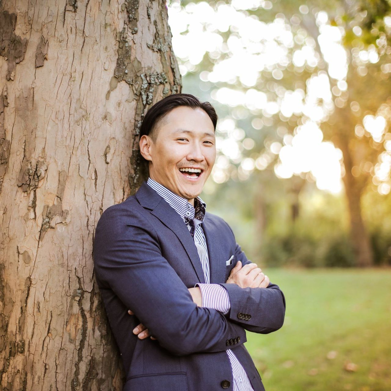 一名西裝革履的男子雙手交叉,斜倚在樹上