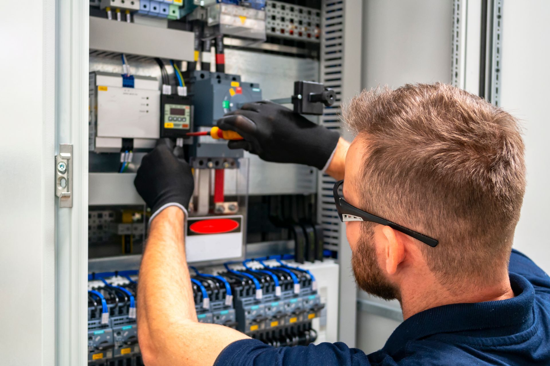 Electrician working on an electrical panel, wearing gloves and glasses.