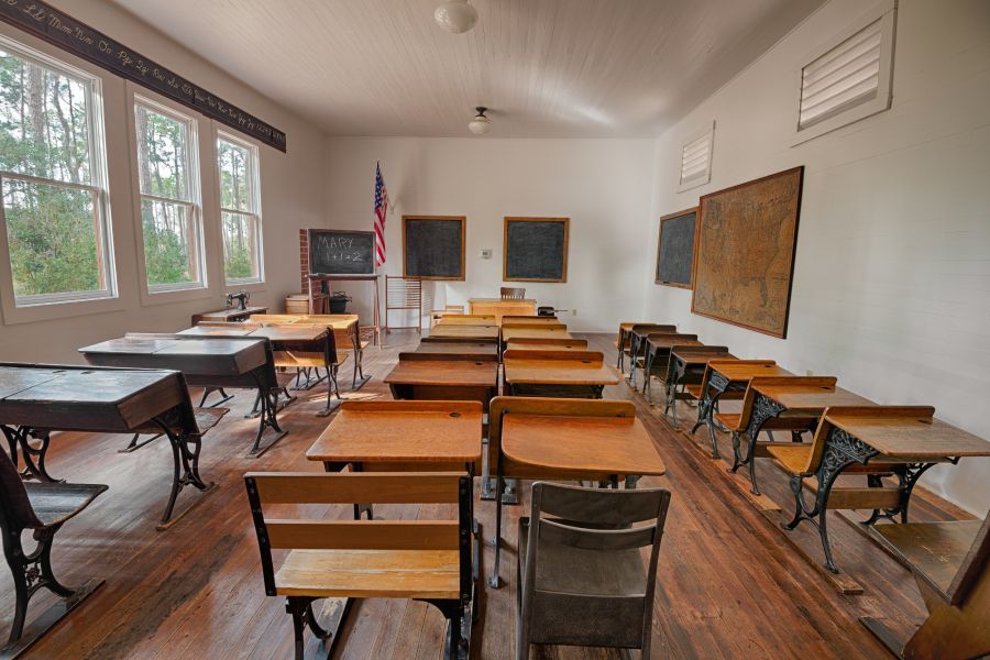 An empty classroom with wooden desks and chairs and chalkboards.