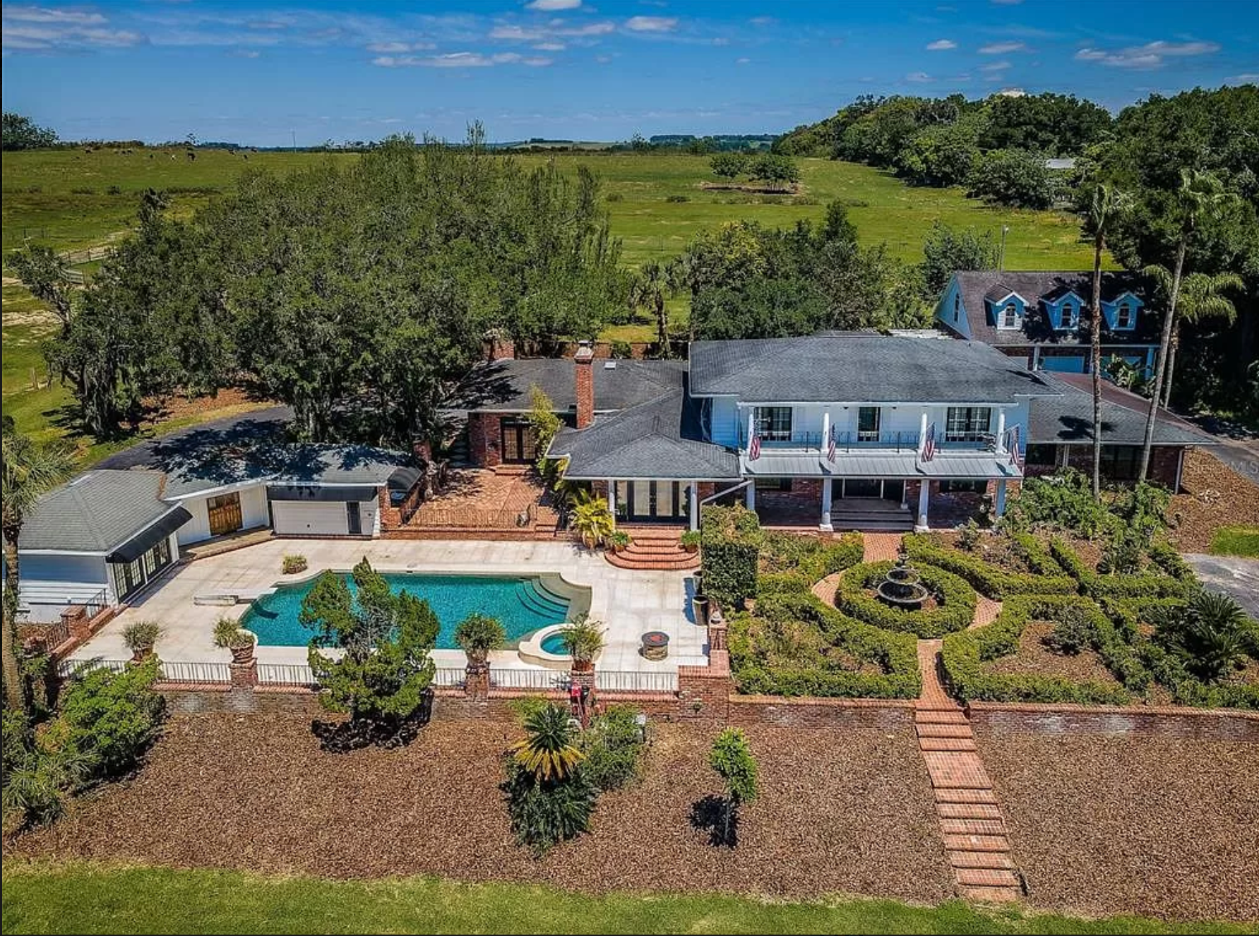 An aerial view of a large house with a swimming pool surrounded by trees.